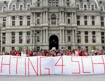 Teachers hold up a large sign in front of City Hall at the protest that reads 'FIGHTING 4 SCHOOLS'