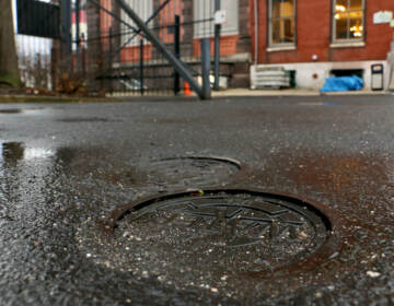 Metal caps marked ''WATER'' are the only evidence of the 400-foot wells beneath the parking lot of the German Society of Pennsylvania on Spring Garden Street. The wells tap the geothermal energy of the earth to heat and cool the society's building. (Emma Lee/WHYY)