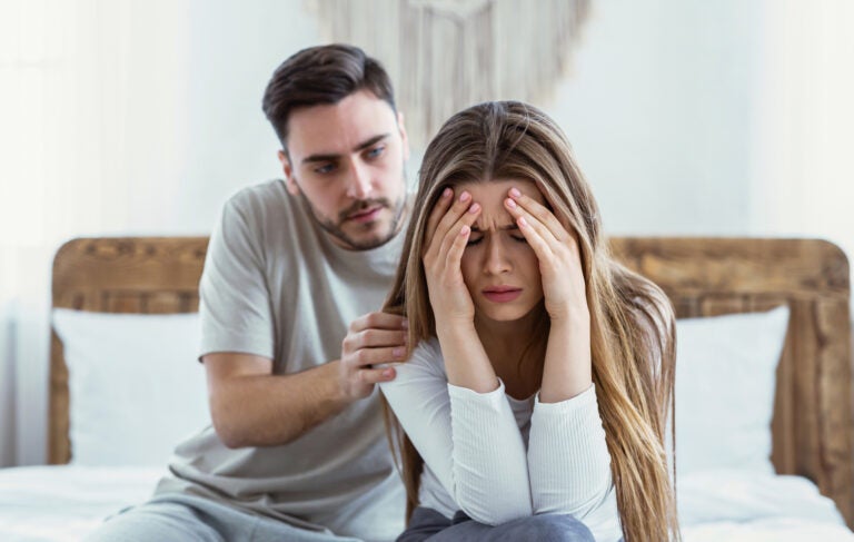 A woman distressed with her head in her hands while a man tries to console her.