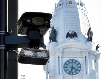 Close-up shot of a speed camera attached to a light pole, with City Hall in the background