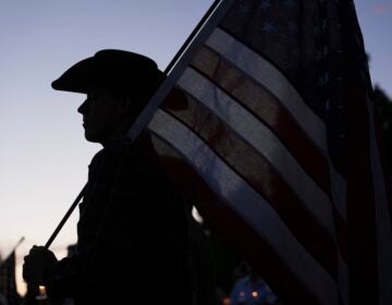A silhouette of a man wearing a cowboy hat holding a large American flag