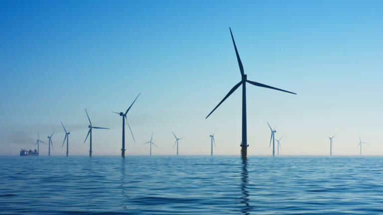 Offshore wind turbines are visible stretching into the distance with blue sky in the background.
