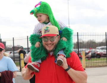 A man holding a small child on his shoulders who is wearing a Phanatic costume
