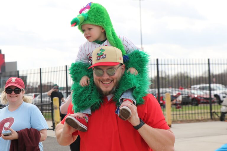 A man holding a small child on his shoulders who is wearing a Phanatic costume