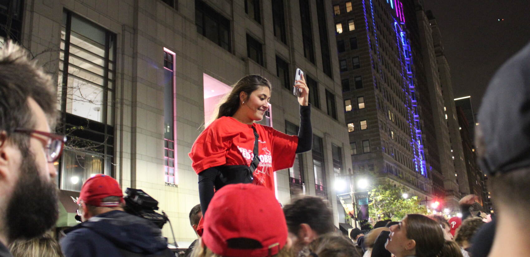 A person in a Phillies shirt stands above a crowd.